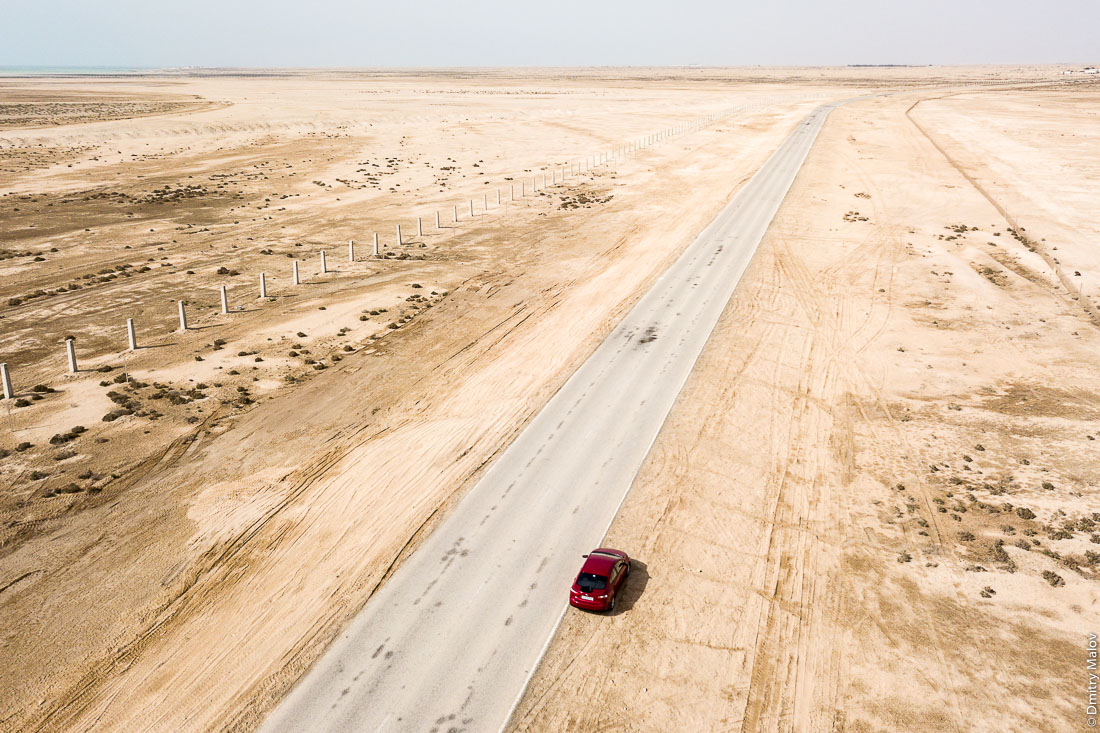 Aerial view of desert, asphalt road and a red car, Madinat ash Shamal near Zubarah, Qatar. Фото с дрона, пустыня, красная машина, Зубарах, район Эш-Шамаль, Катар  