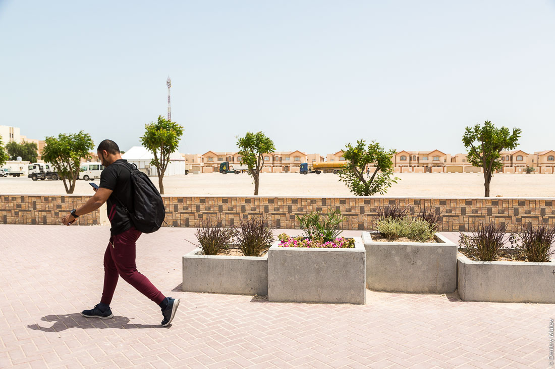 Мужчина идёт по мощенной улице с клумбами, город Аль-Хор (Эль-Хаур), Катар. A man walks along a cobbled tiles street with flower beds, Al Khor city, Qatar.